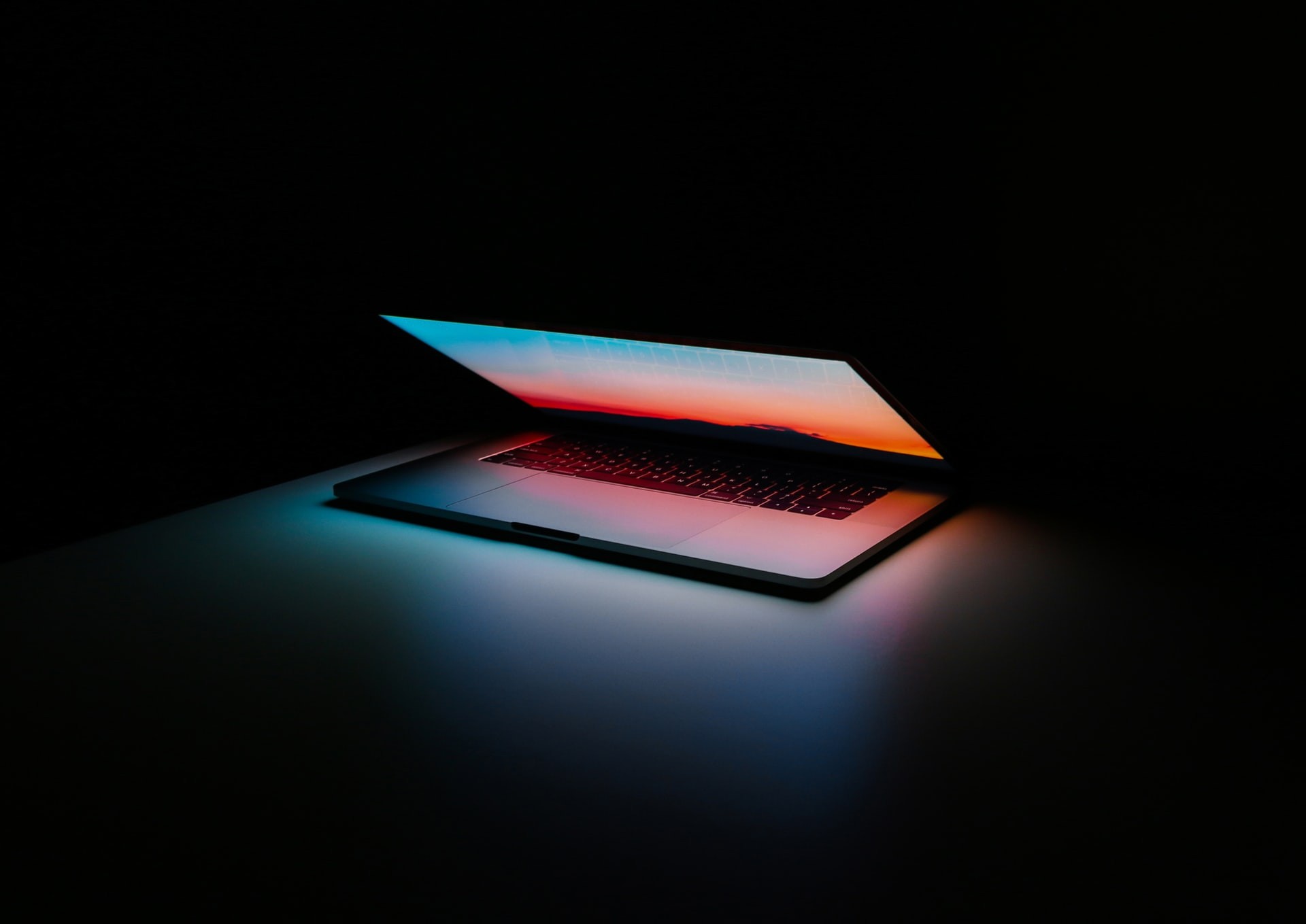 A sleek laptop reflecting a vibrant sunset in a pitch black room.